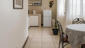 A compact kitchen with a microwave, refrigerator, and a dining area with a table and chairs. - Casa Cafetal Aeropuerto (Alajuela)