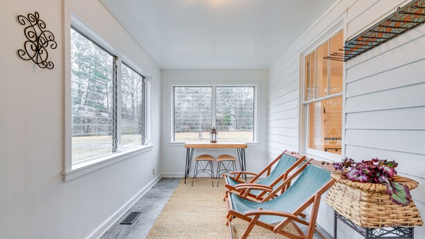 A covered porch with a table and chairs, a wicker basket with flowers, and a view of trees through the windows. - Charming Virginia Retreat w/ Covered Porch & Yard! (Farmville)