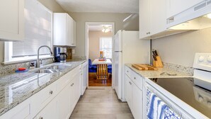A kitchen with white cabinets, a granite countertop, a sink, a stove, and a dining area with blue chairs. - Pet-Friendly Georgia Retreat w/ Fire Pit & Porch! (Forest Park)