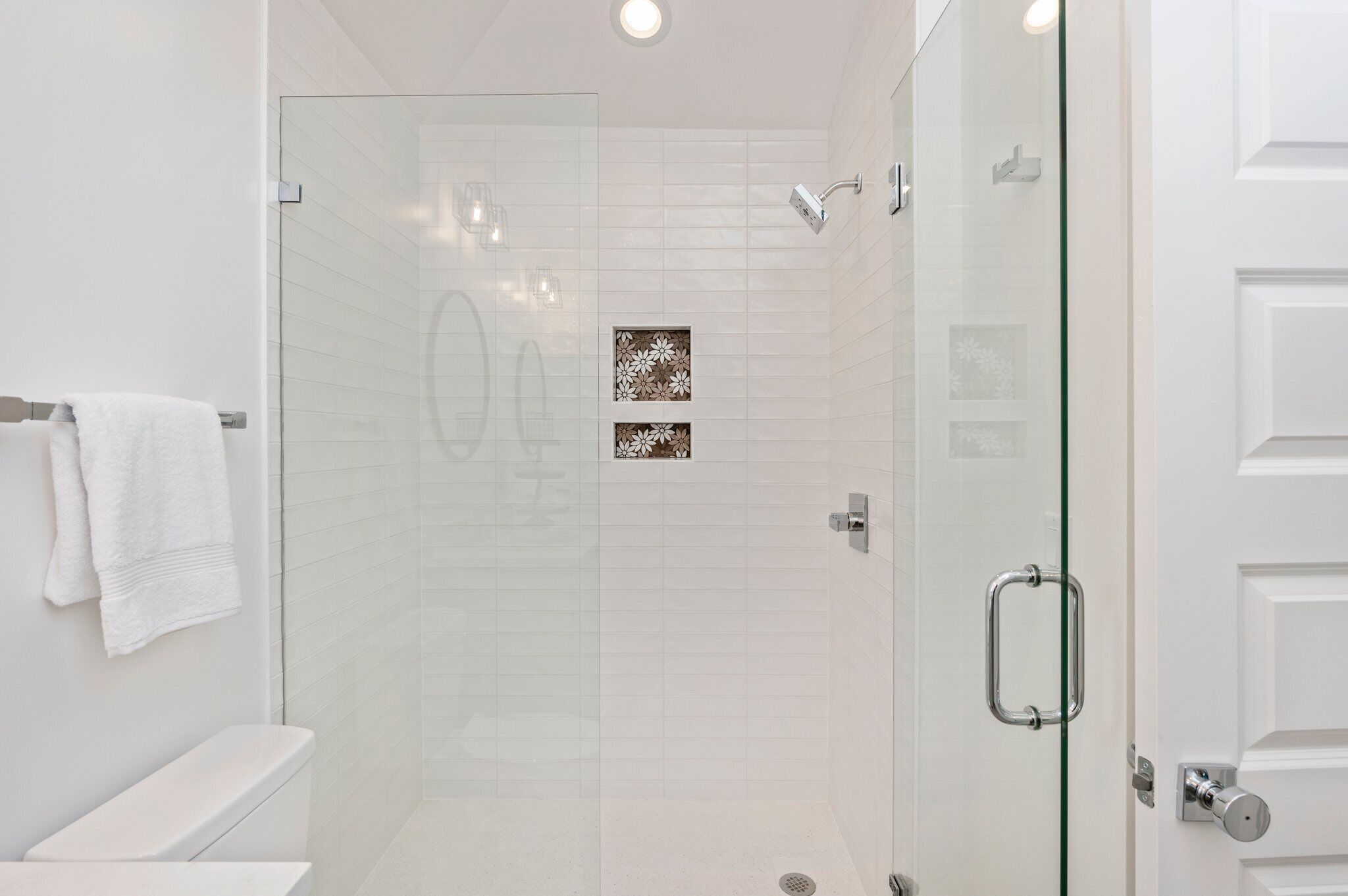 A modern bathroom with a glass-enclosed shower, white tiles, and a toilet with a white towel.