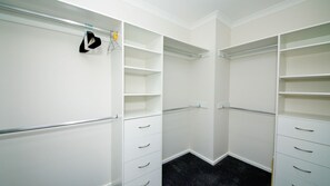 Een inloopkast met witte planken, meerdere lades en een kledingroede.
