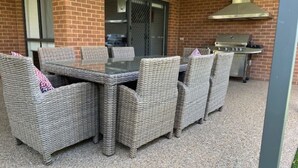 Een terras met een rieten tafel en stoelen, een barbecue en een bakstenen muur.