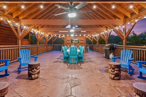 An outdoor covered patio with wooden beams, string lights, and blue Adirondack chairs.