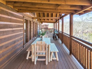 A wooden deck with a table and chairs, a railing, and a view of trees.