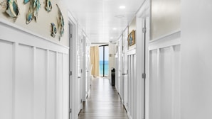 A hallway with white walls and doors, leading to a room with a view of the ocean.