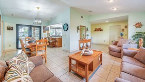 A spacious living room with a dining area, a kitchen in the background, and a large window. - Marco Island Home w/ Private Pool & Water Views! (Marco Island)