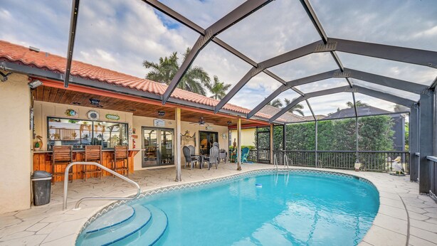 A covered swimming pool with a bar area, outdoor seating, and a view of palm trees. - Marco Island Home w/ Private Pool & Water Views! (Marco Island)