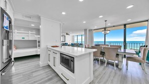 Una cocina moderna con una isla central, comedor con sillas y vistas al océano.