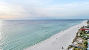 En strand med en brygga som sträcker sig ut i havet, en sandstrand och byggnader längs kustlinjen.