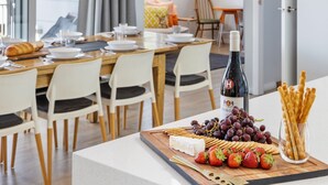 A dining area with a wooden table set for a meal, featuring a bottle of wine, grapes, strawberries, and crackers.