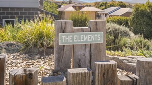 A sign reading "THE ELEMENTS" in a garden setting with a stone wall and greenery.