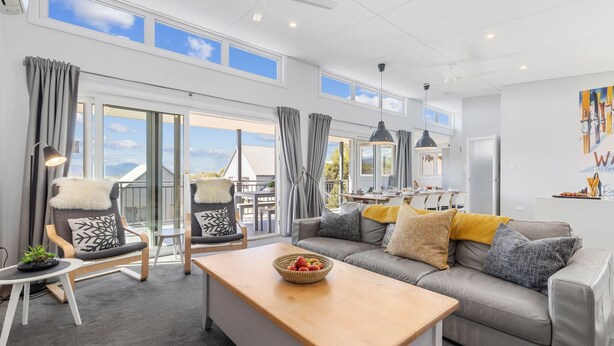 A modern living room with a grey sofa, a wooden coffee table, and a dining area with a table and chairs.