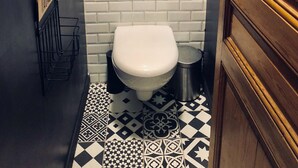 Un baño pequeño con un inodoro blanco, una pared de azulejos blancos, una cita enmarcada y un cerdito rosa en la pared.
