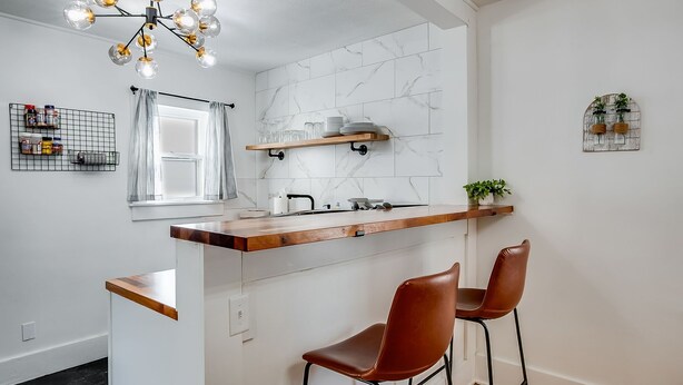 Una cocina moderna con encimera de madera, dos taburetes de bar, una lámpara colgante y una ventana con cortinas.