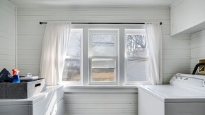 Un lavadero con dos lavadoras, una secadora y una ventana con cortinas.