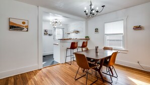 Un comedor con una mesa y sillas de madera, una araña y vista a la cocina.
