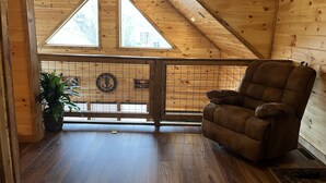 Un interior de madera con techo alto, un ventanal grande, un sillón mullido y una planta en maceta.
