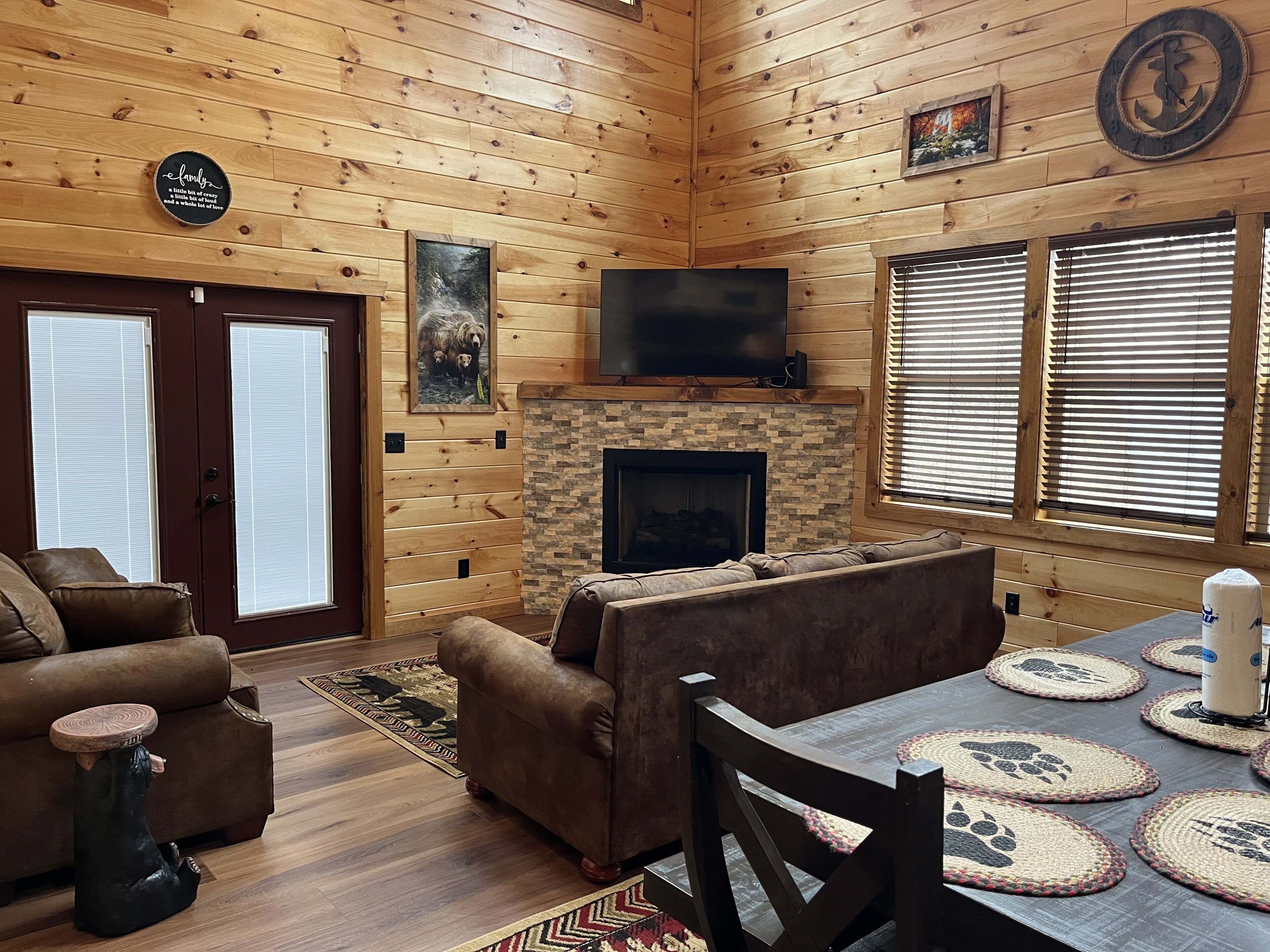 A cozy cabin interior with a fireplace, wooden walls, a television, and a dining area with placemats.