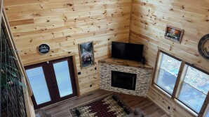 Un interior de cabaña acogedor con chimenea, paredes de madera, televisor y sofá.