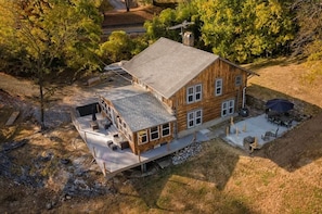 A two-story log cabin with a deck, outdoor seating, and a chimney.