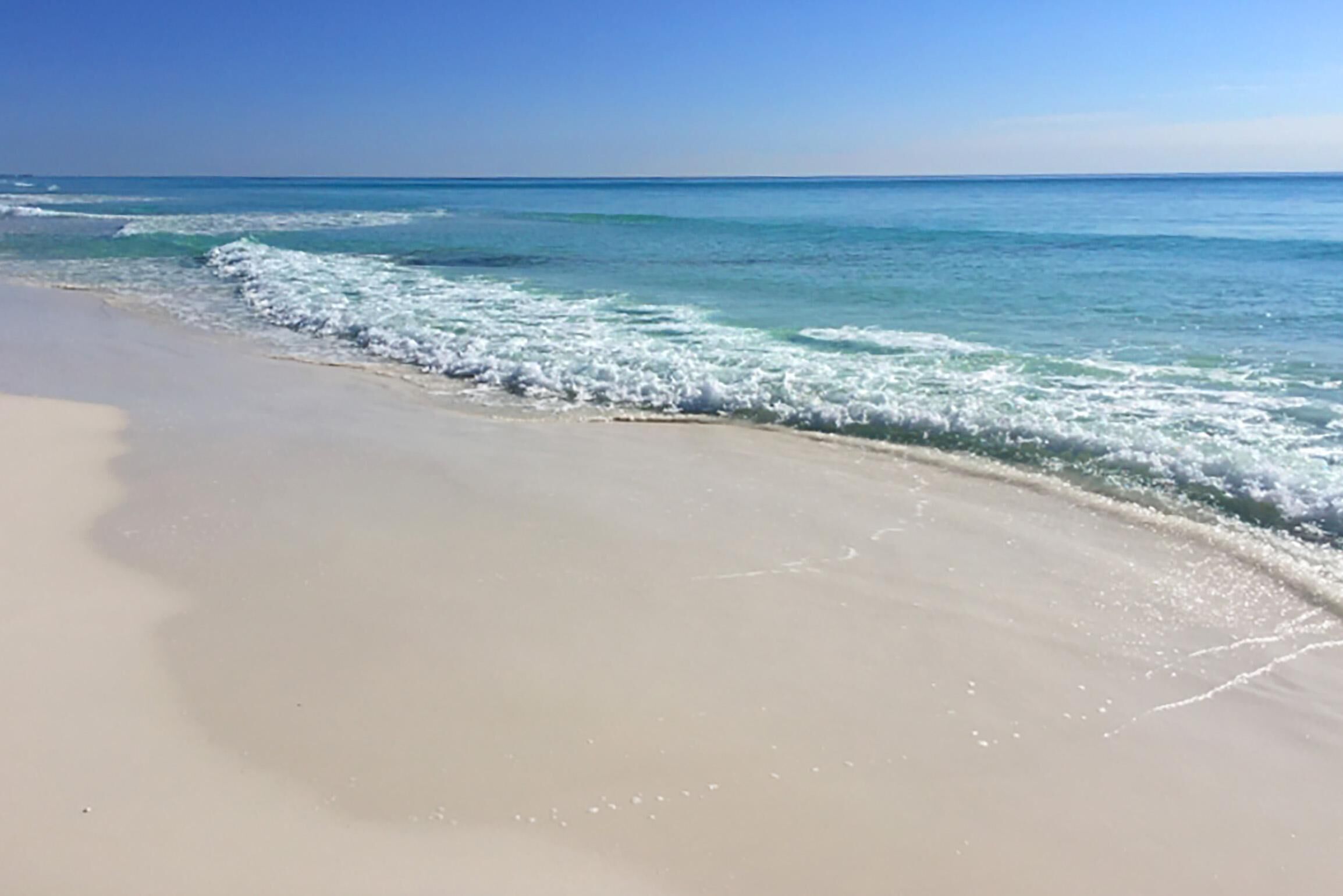A beach with clear blue water and a sandy shore.