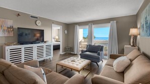 Un salon avec un téléviseur, des canapés, une table basse et une vue sur l’océan.