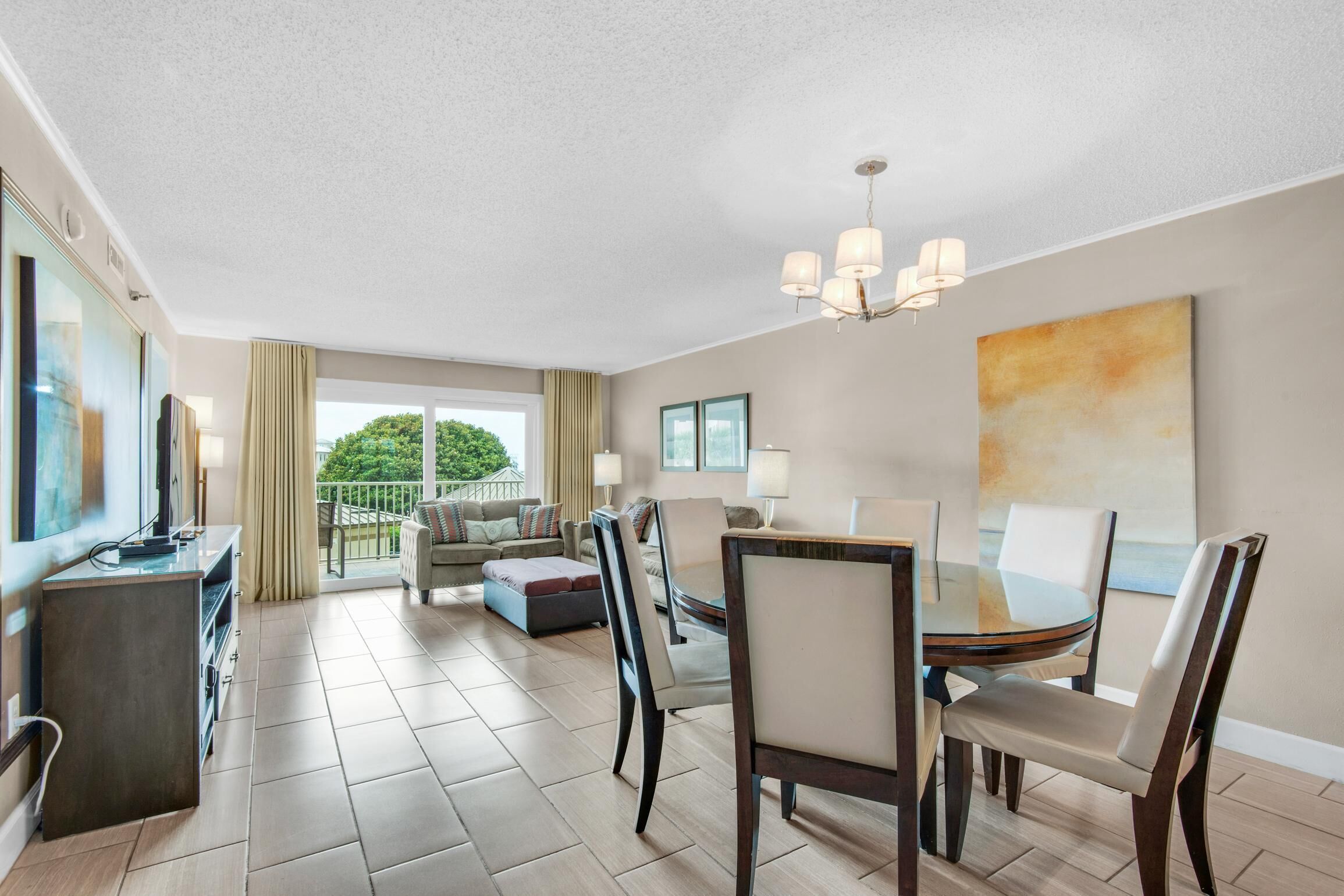 A modern hotel room with a dining area, a balcony with a view, and a large painting on the wall.