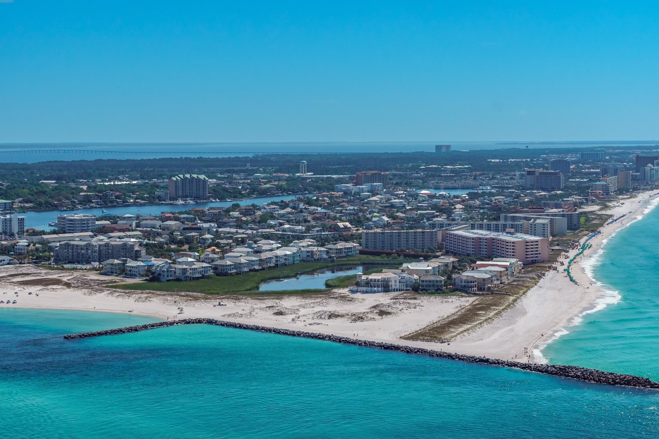 An aerial view of a coastal city with a beachfront, residential buildings, and a bridge in the distance.