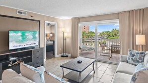 A hotel room with a TV, sofa, coffee table, and a balcony with outdoor seating. - Ocean 214 at The Islander (Destin)
