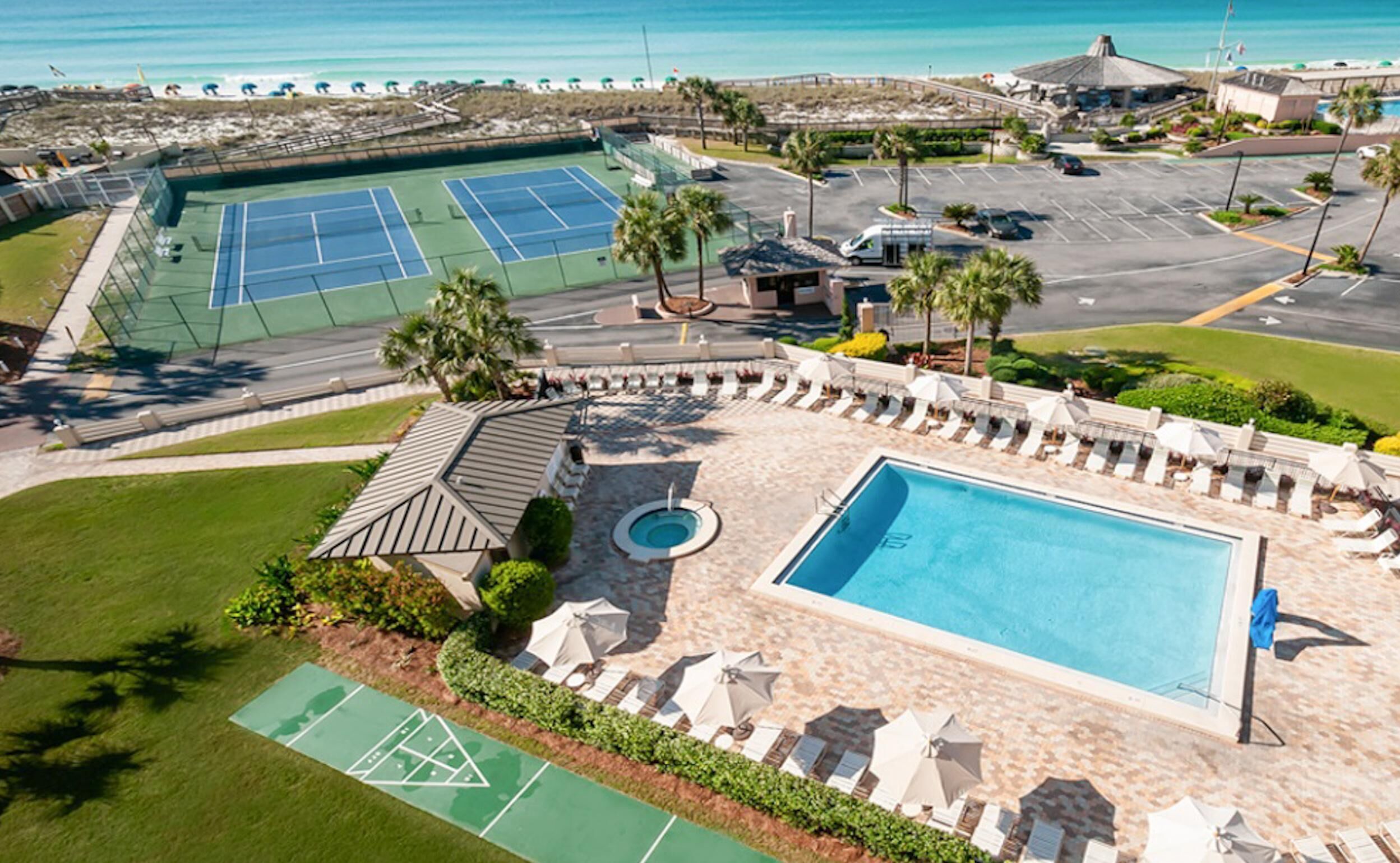 An aerial view of a resort with a swimming pool, tennis courts, and a parking area.