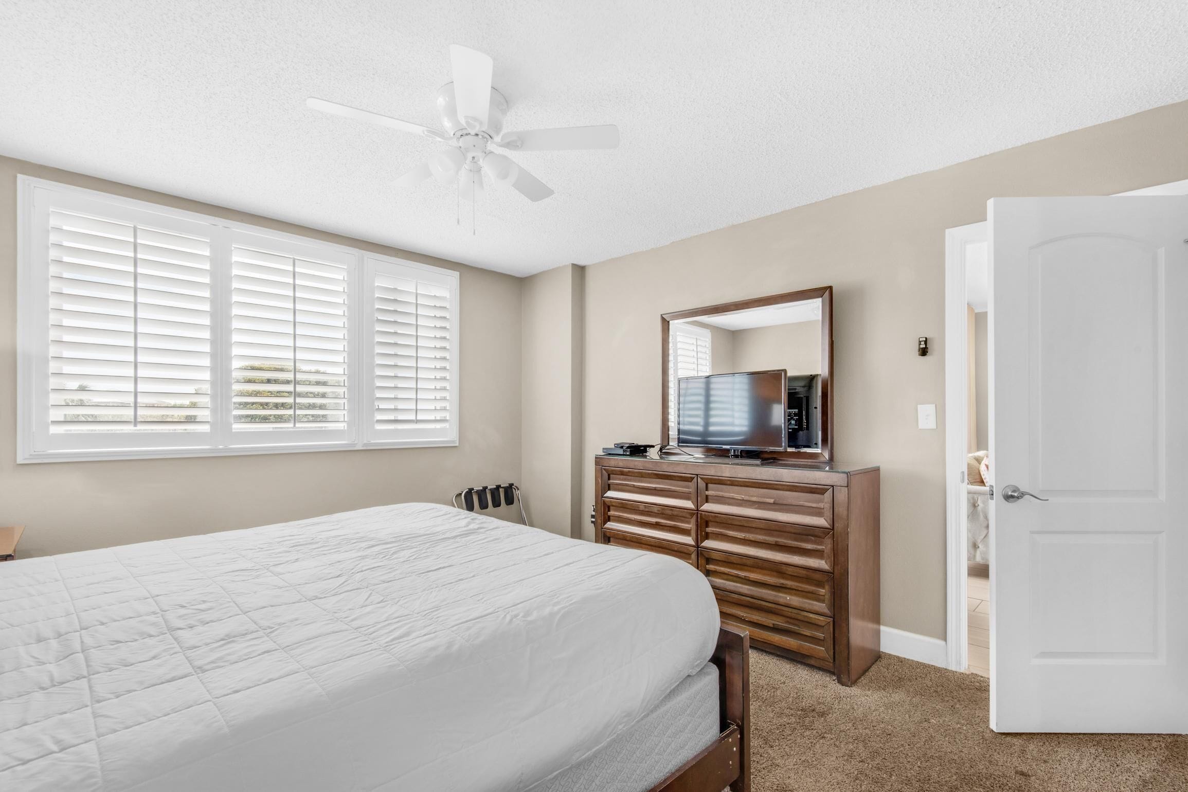 A bedroom with a bed, dresser, TV, and ceiling fan.