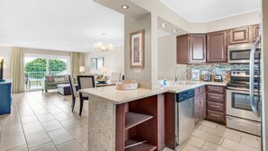 A modern kitchen with a central island, built-in appliances, and a dining area with a view to the outdoors. - Ocean 214 at The Islander (Destin)
