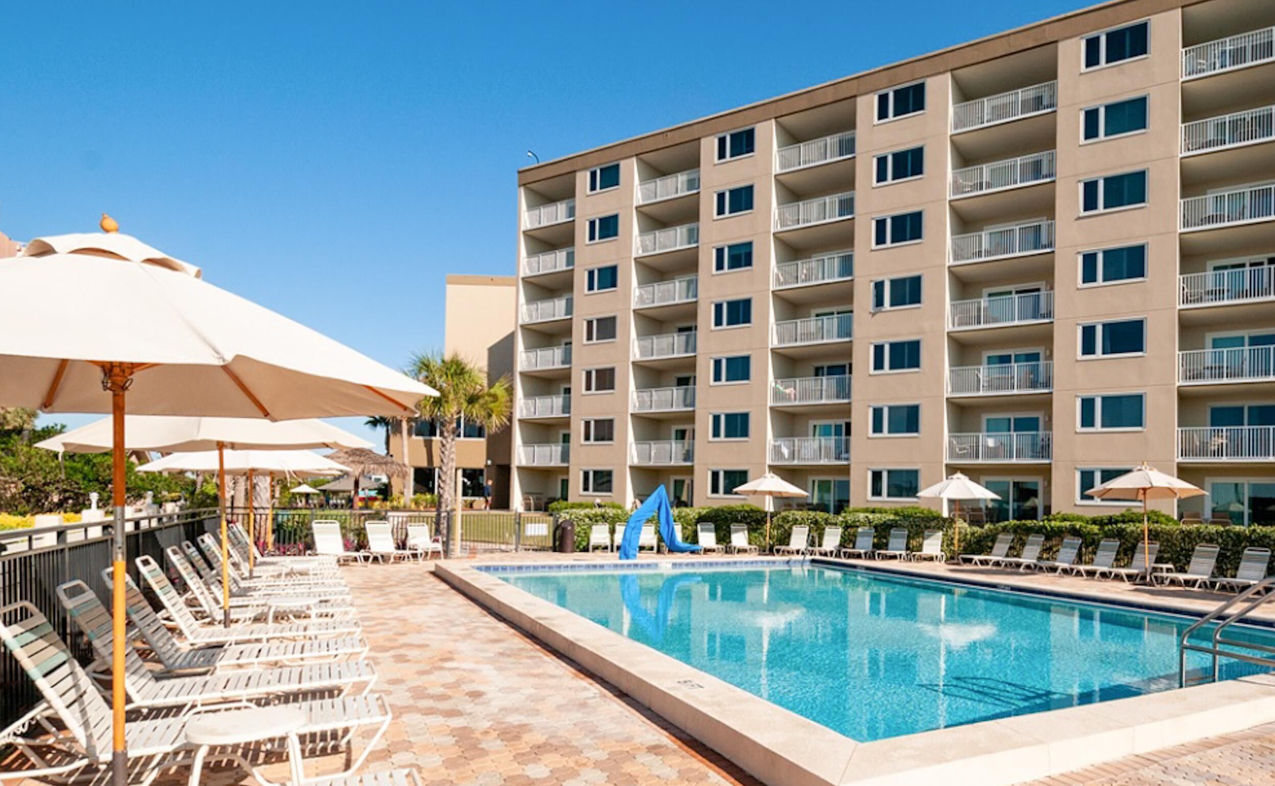 A hotel with a swimming pool, sun loungers, and umbrellas.