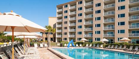 A hotel with a swimming pool, sun loungers, and umbrellas.