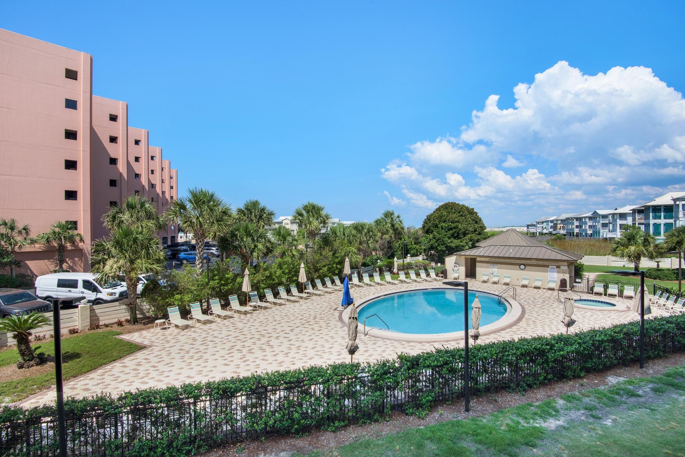 A hotel with a pool area, palm trees, and a clear blue sky.