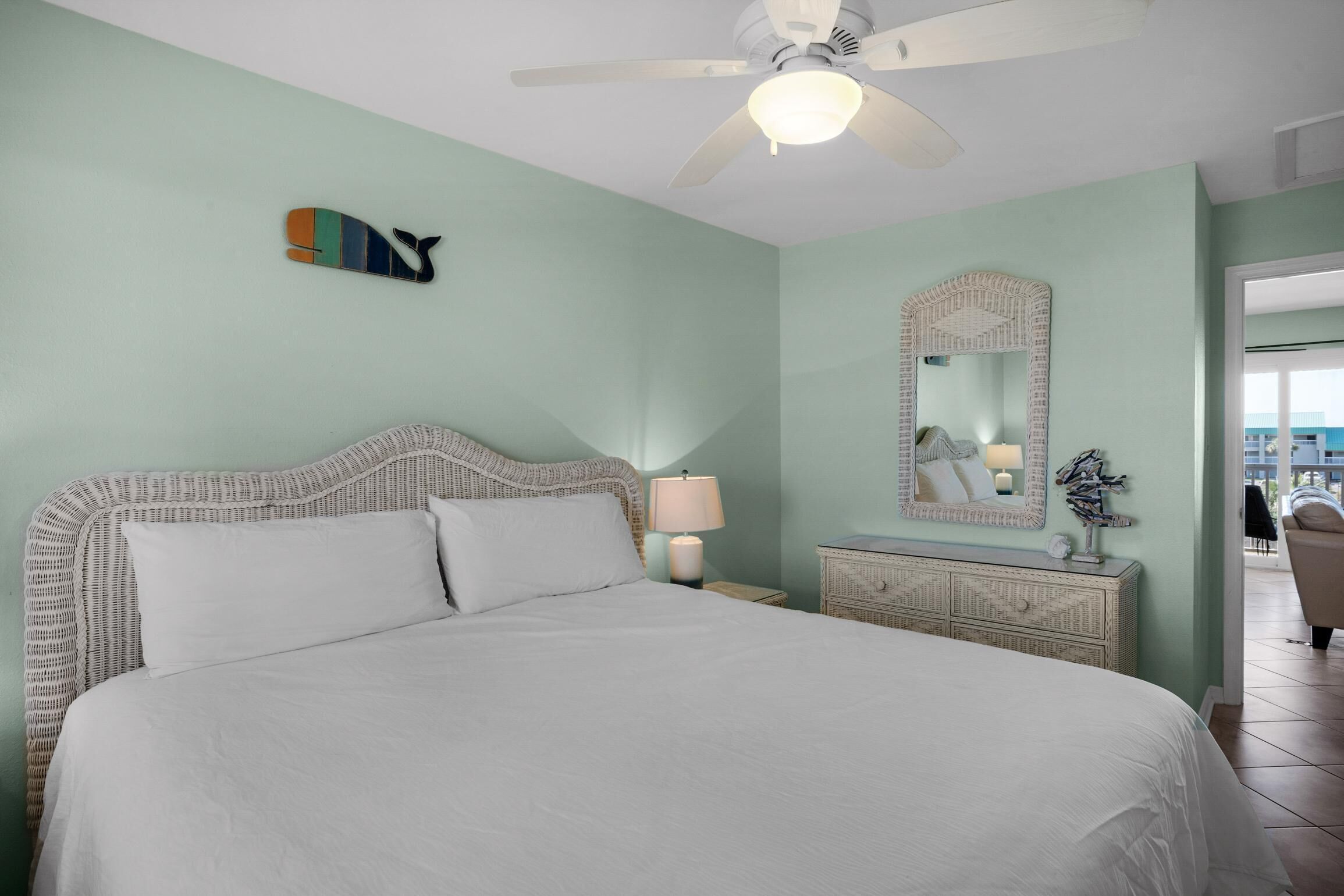 Un dormitorio ordenado con cama, lámpara de noche, cómoda y un espejo de pared.