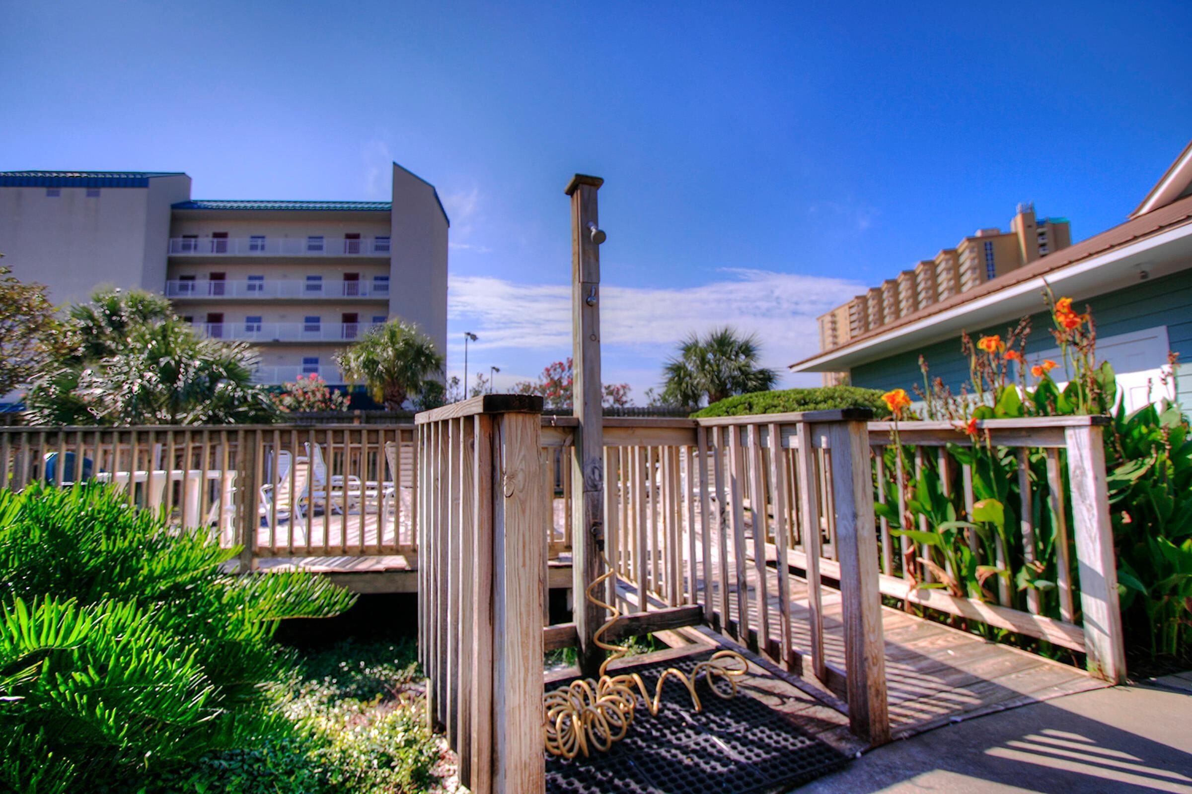 A wooden deck with a metal spiral staircase, surrounded by lush greenery and a clear blue sky.