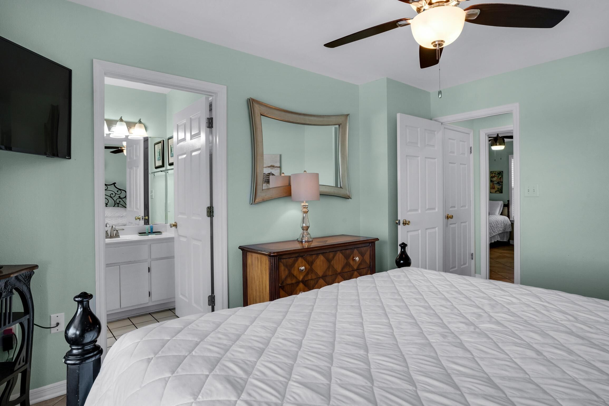 Une chambre avec un grand lit, un ventilateur de plafond, une commode et un miroir.