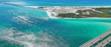 An aerial view of a coastal area with a bridge, clear turquoise waters, and a small island with vegetation.