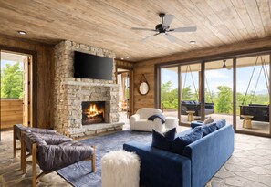 Un salon chaleureux avec une cheminée en pierre, des fauteuils en cuir, un canapé bleu et un grand téléviseur.