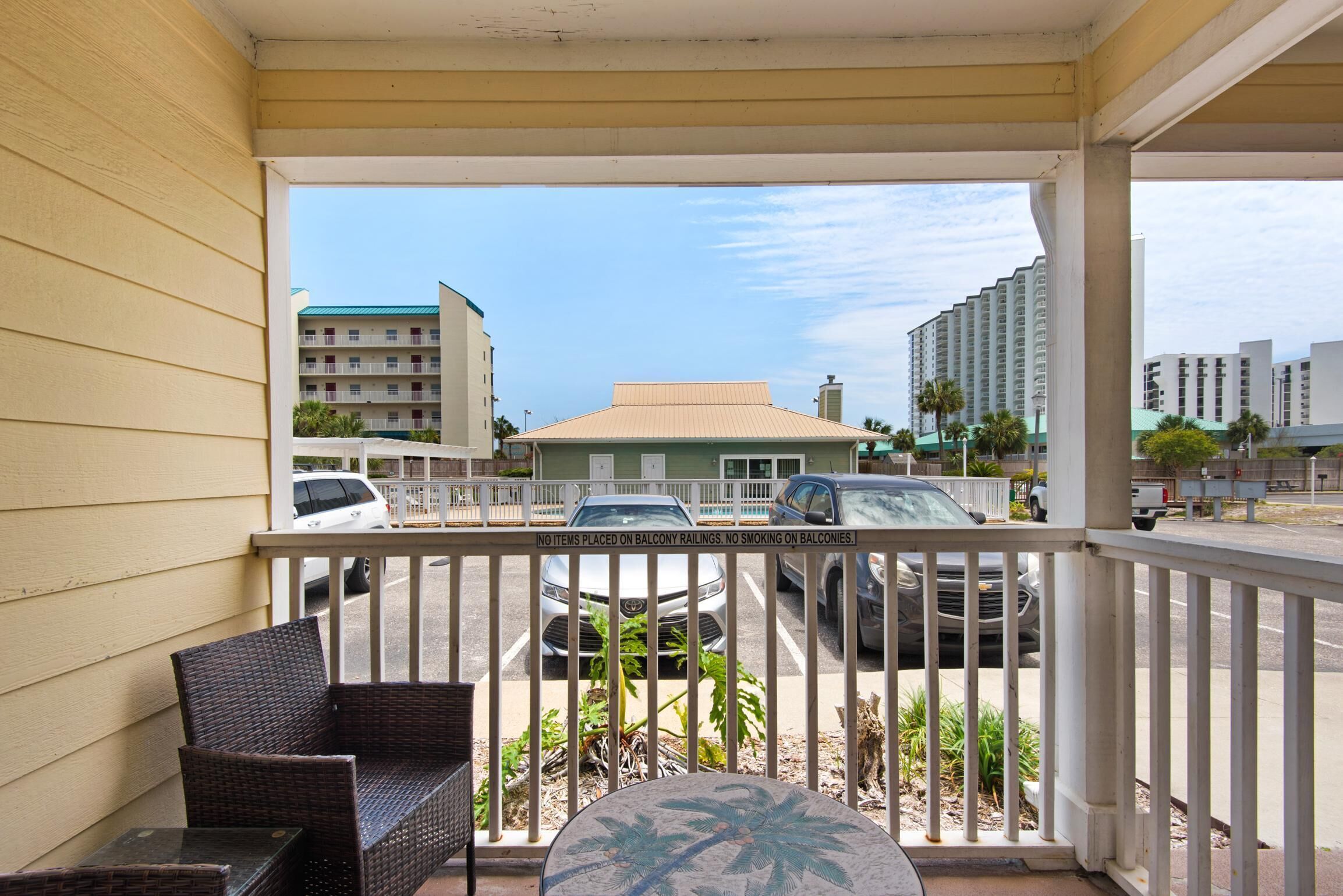 A balcony with wicker furniture and a view of a parking lot and buildings.