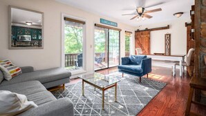 A living room with a gray sofa, a blue armchair, a glass coffee table, and a wooden bench. There is a large mirror on the wall, a ceiling fan, and a sign that reads "LAKE HOUSE". - Lakefront Getaway, Private Dock, Porch, and Fishing! (Roxboro)