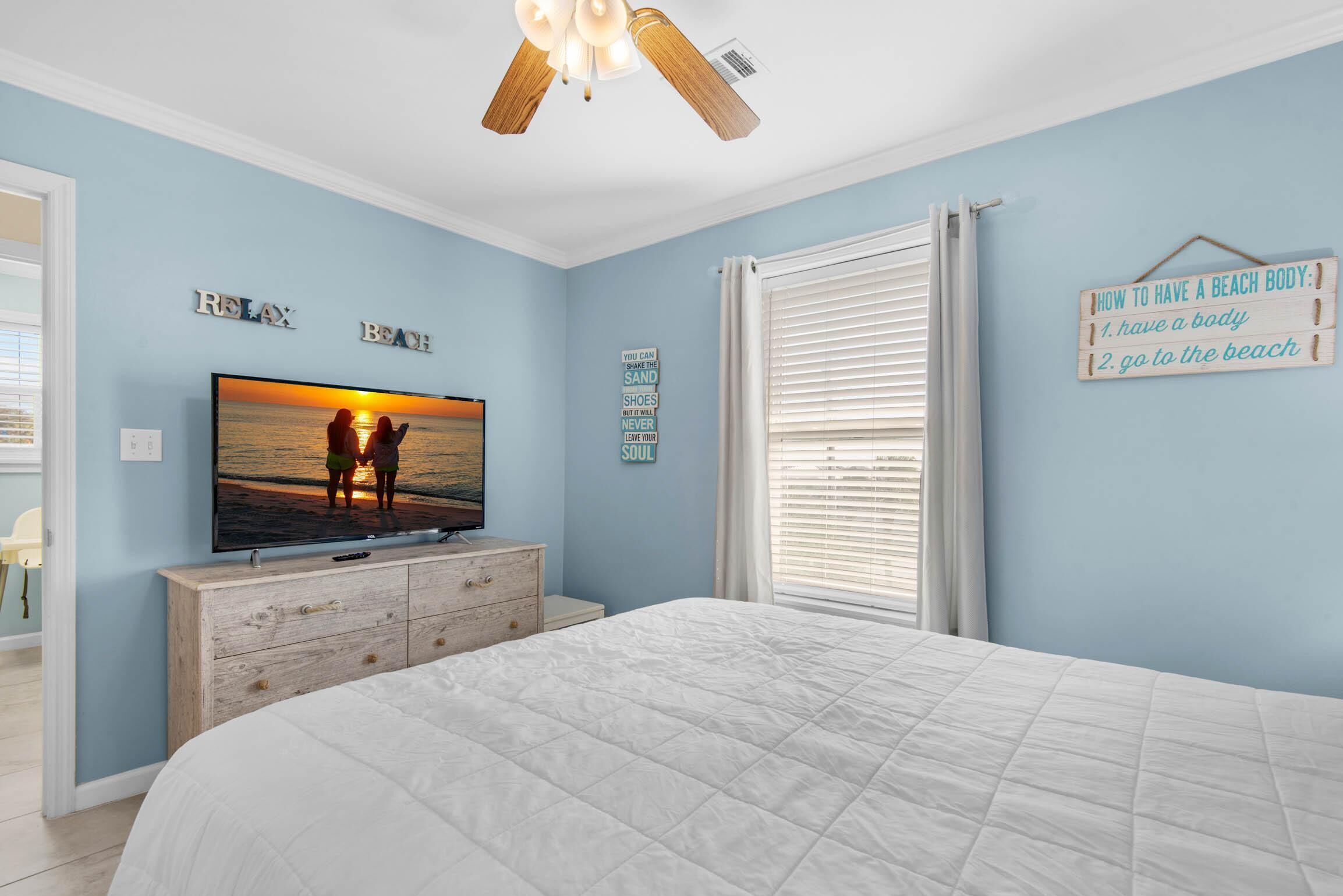 A bedroom with a bed, a TV on a dresser, and a ceiling fan.