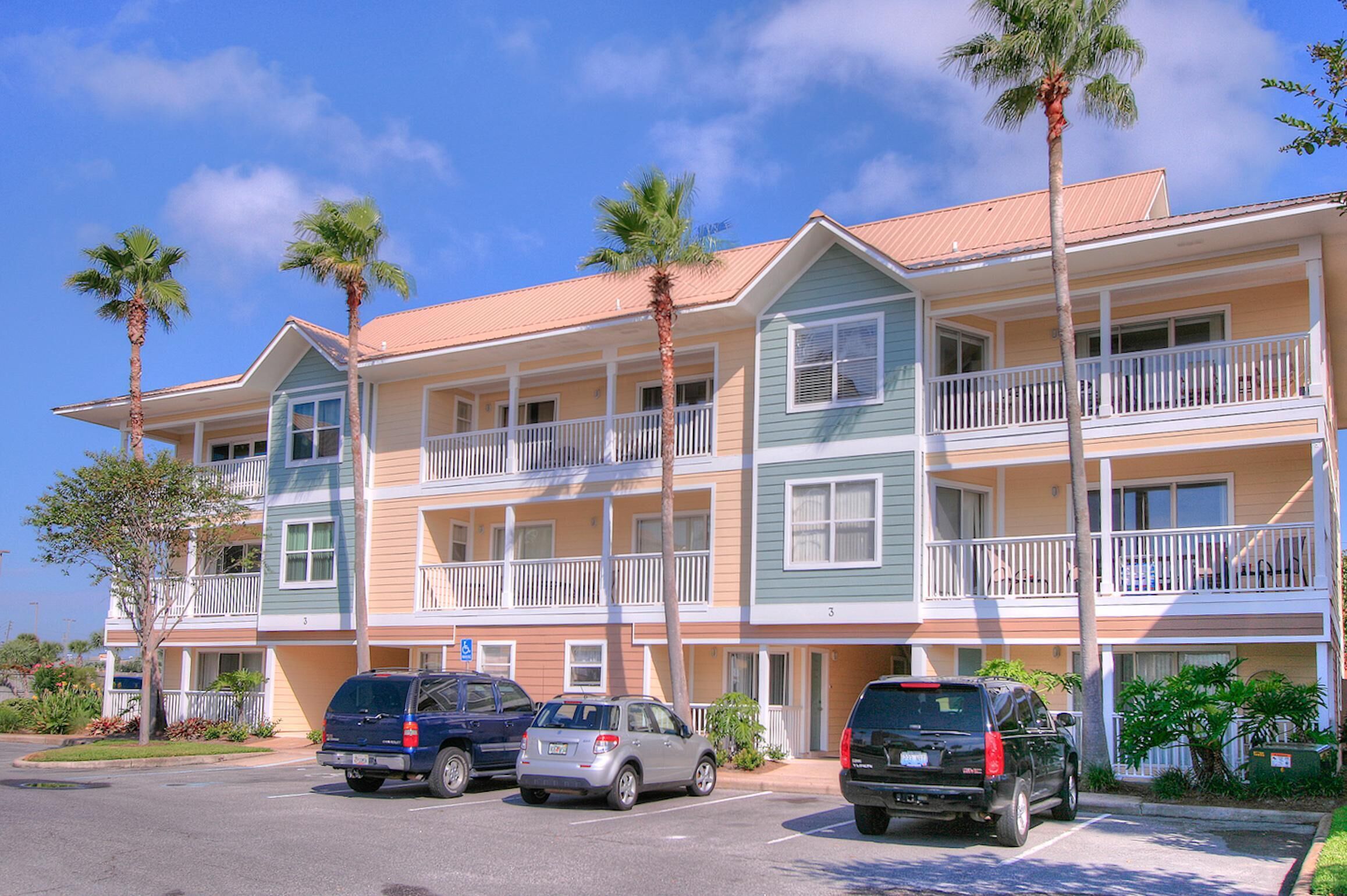 A multi-story hotel with balconies, parking spaces, and palm trees.
