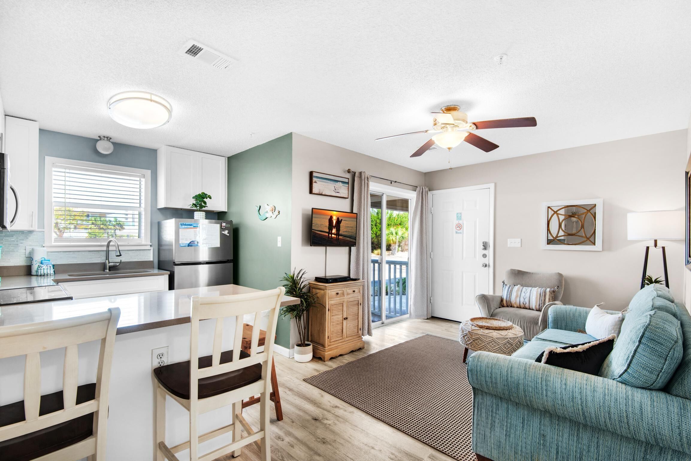 A modern kitchen with a dining area, a living room with a sofa, and a ceiling fan.