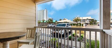 A balcony with a table and chairs, a view of a parking area, and buildings in the background.