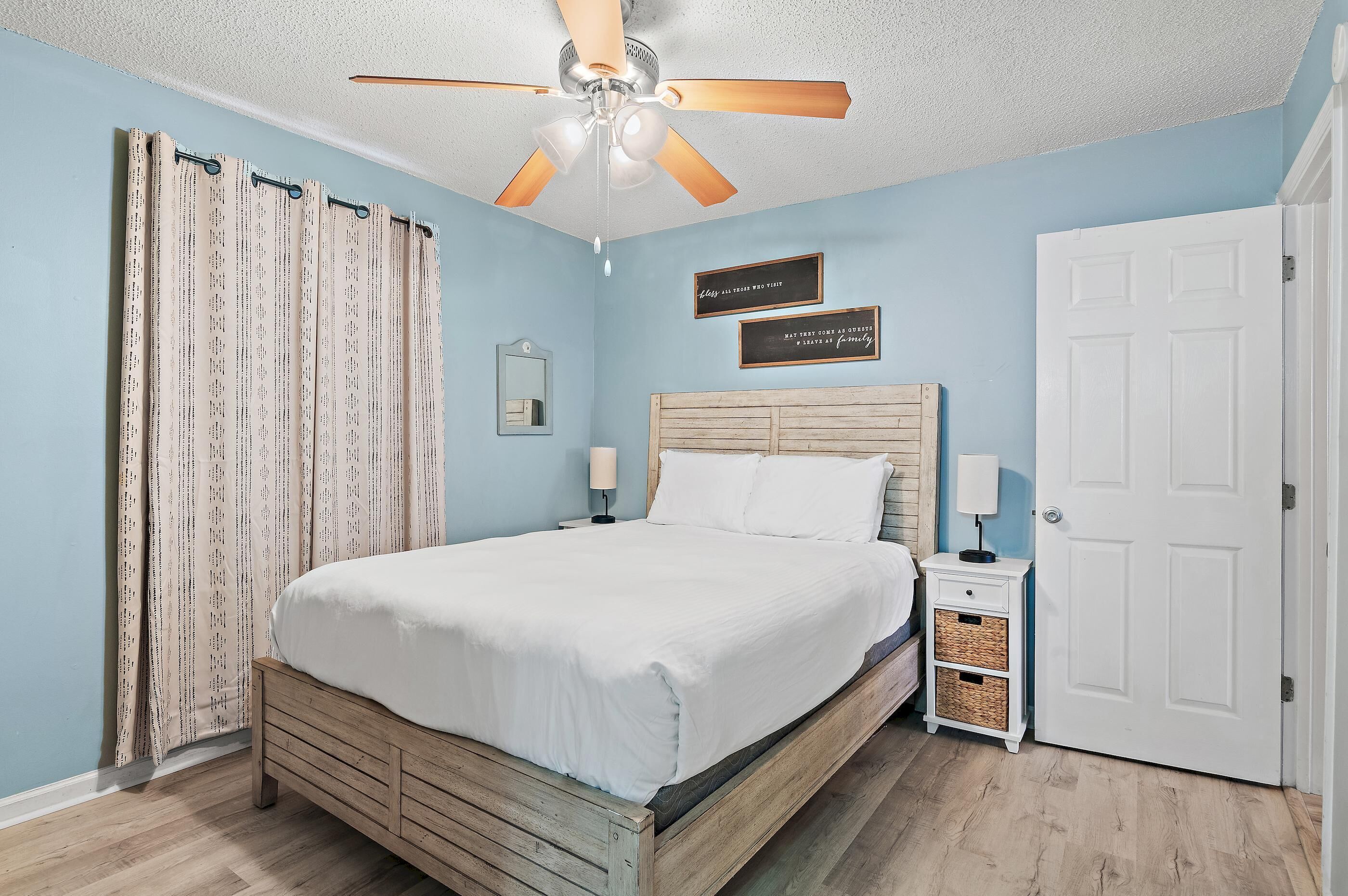 A bedroom with a wooden bed, a ceiling fan, a white door, and a nightstand with a lamp.