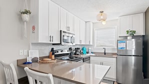 A modern kitchen with white cabinets, stainless steel appliances, and a central island with seating. - St Martin Beachwalk Villas 112 (Destin)