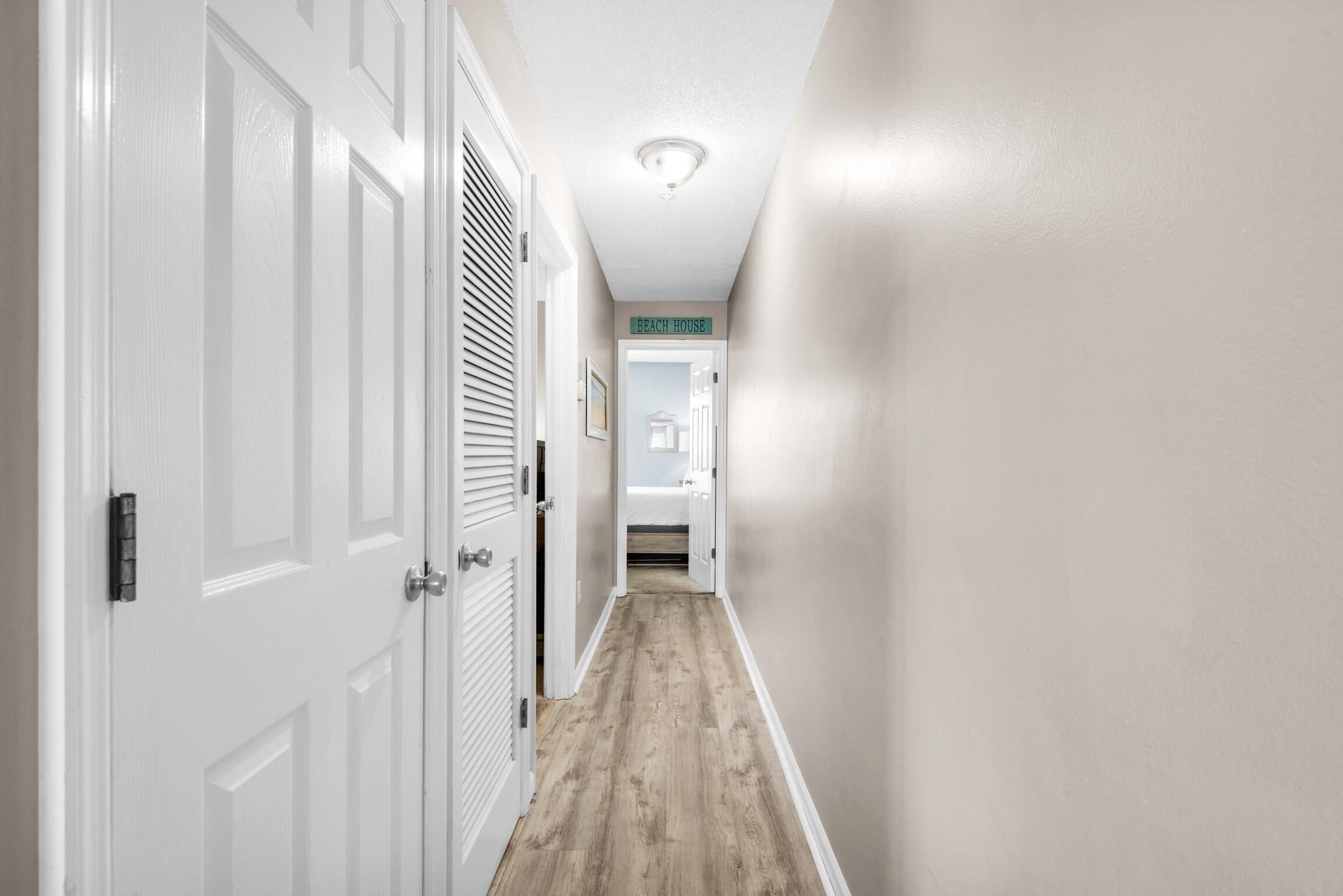A hallway with white doors, a wooden floor, and a sign reading "BEACH HOUSE".