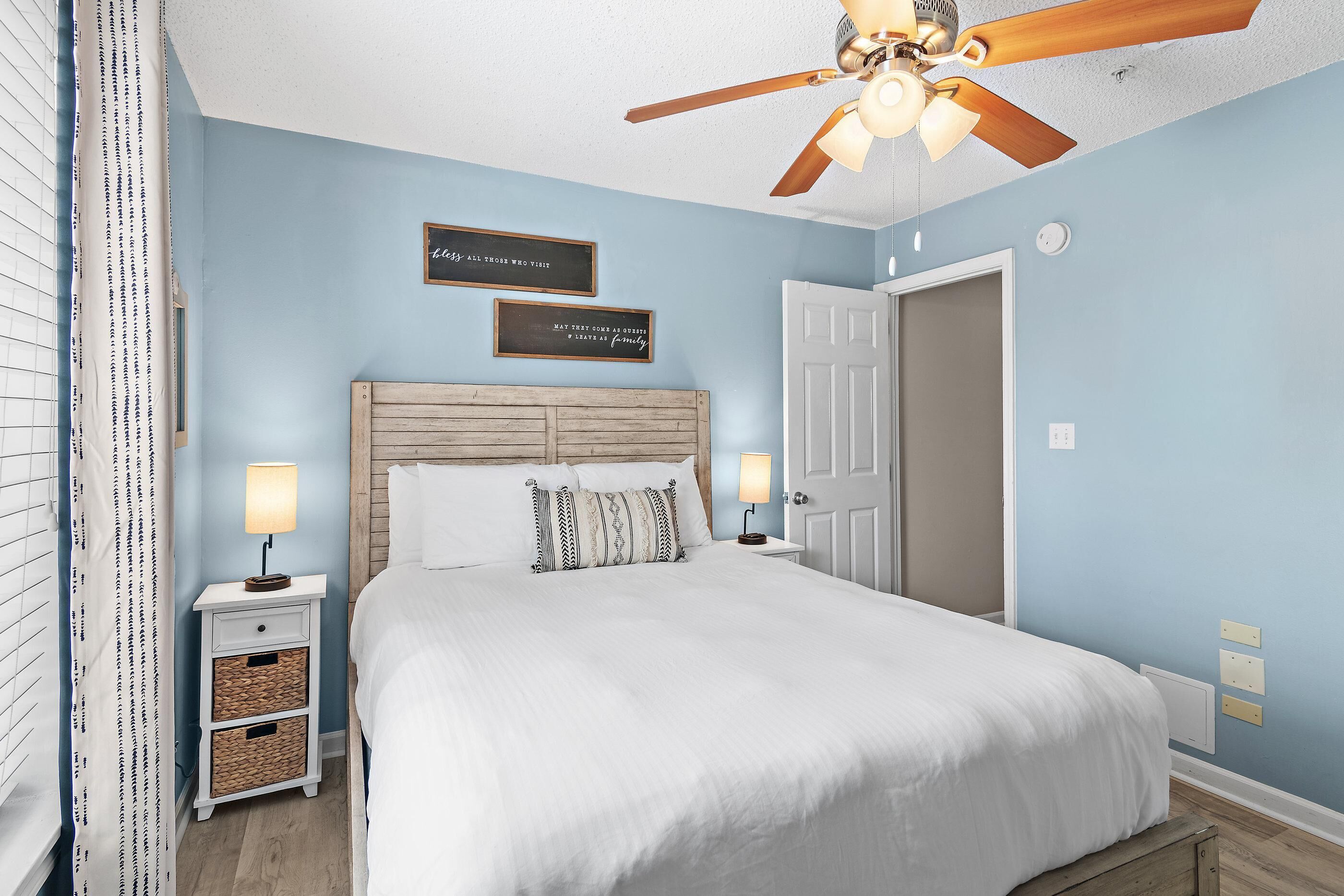 A bedroom with a bed, two bedside tables, a ceiling fan, and two wall-mounted light fixtures.